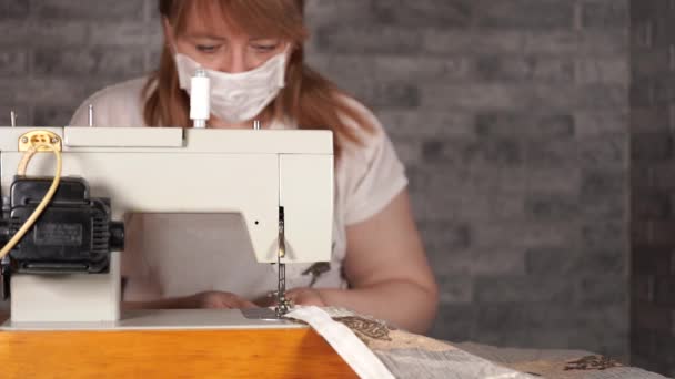 Primer plano de la mujer adulta costura cortina, utilizando la máquina de coser. Joven costurera en máscara médica trabajando en la máquina de coser en casa . — Vídeo de stock