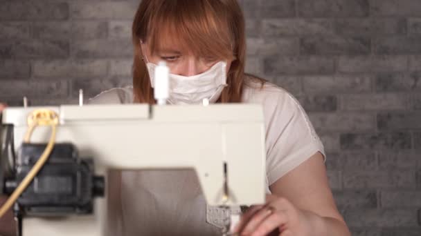 성인 여성 이 바느질 기계를 사용하여 커튼을 꿰매는 것을 마무리하는 것입니다. 가정에서 재봉틀을 만들고 있는 의료용 마스크를 쓰고 있는 청소년의 재봉틀. — 비디오