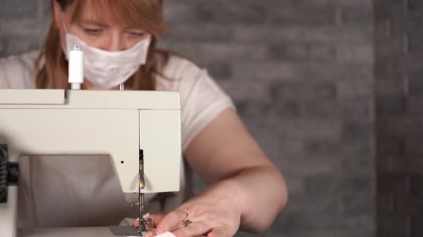 Close-up van volwassen vrouw naaien gordijn, met behulp van naaimachine. Jonge naaister in medisch masker werkt aan naaimachine thuis. — Stockvideo