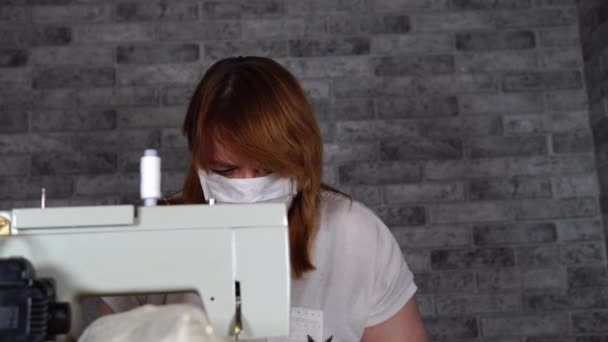 Primer plano de la mujer adulta costura cortina, utilizando la máquina de coser. Joven costurera en máscara médica trabajando en la máquina de coser en casa . — Vídeo de stock