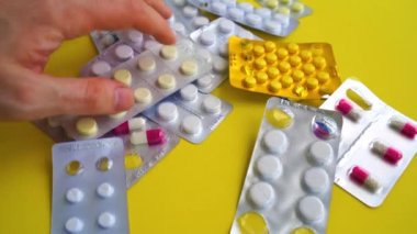 Sarı arka planda çeşitli tabletlerle dolu tıbbi kabarcık paketlerini kapatın. Erkekler uygun tablet paketini elle seçiyorlar. Çeşitli hastalıkların önlenmesi kavramı.