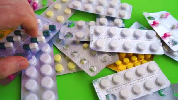 Närbild av blisterförpackningar med tabletter på grön bakgrund. Förpackningar med olika tabletter. Begreppet hot om olika sjukdomar. — Stockvideo