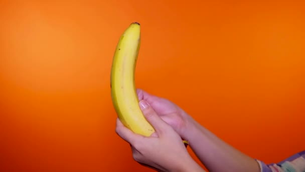 Närbild av kvinna peeling banan på orange bakgrund. Kvinnors händer skalar den mogna frukten. — Stockvideo