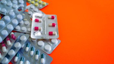 Turuncu arka planda tabletleri olan tıbbi su toplayıcılarını kapatın. Çeşitli tabletlerle dolu paketler. Çeşitli hastalık tehdidi kavramı.