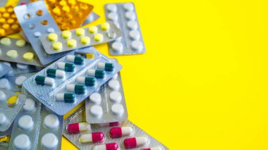 Sarı arka planda tabletleri olan tıbbi su toplayıcılarını kapatın. Çeşitli tabletlerle dolu paketler. Çeşitli hastalık tehdidi kavramı.