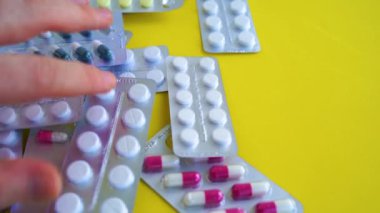 Sarı arka planda çeşitli tabletlerle dolu tıbbi kabarcık paketlerini kapatın. Erkekler uygun tablet paketini elle seçiyorlar. Çeşitli hastalıkların önlenmesi kavramı.