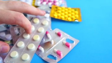Mavi arka planda çeşitli tabletlerle dolu tıbbi kabarcık paketlerini kapatın. Erkekler uygun tablet paketini elle seçiyorlar. Çeşitli hastalıkların önlenmesi kavramı.