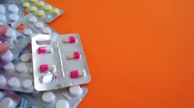 Turuncu arka planda çeşitli tabletlerle dolu tıbbi kabarcık paketlerini kapatın. Erkekler uygun tablet paketini elle seçiyorlar. Çeşitli hastalıkların önlenmesi kavramı.