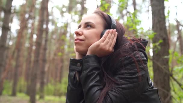 Szczęśliwa młoda kobieta słuchająca muzyki, siedząca na lodzie w lesie. Dorosła samica cieszy się odpoczynkiem na świeżym powietrzu. — Wideo stockowe
