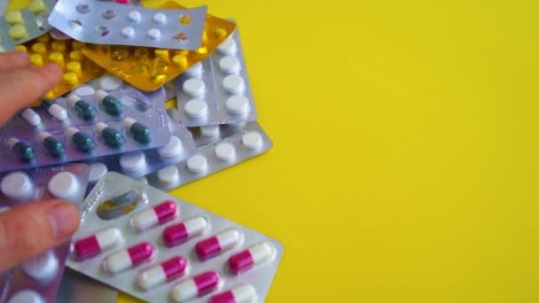 Närbild av blisterförpackningar med olika tabletter på gul bakgrund. Mans hand välja lämplig förpackning med tabletter. Begreppet förebyggande av olika sjukdomar. — Stockvideo