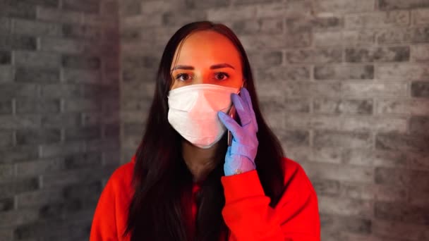 Hübsche junge Frau in medizinischer Maske und Handschuhen, die auf einem grauen Backsteinhintergrund über Coronavirus spricht. — Stockvideo