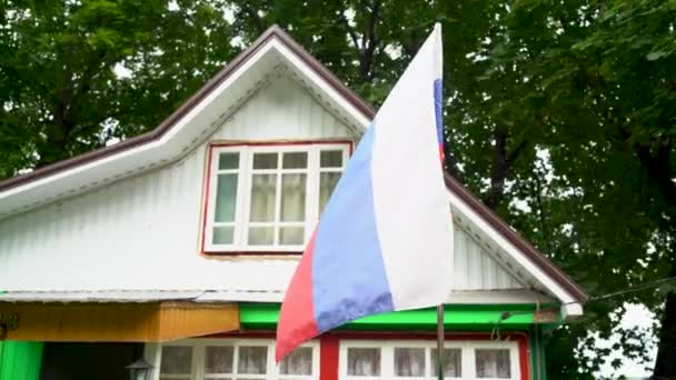 Rusya bayrağı bir kır evinin arka planında rüzgârda dalgalanmakta. — Stok video