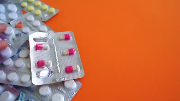 Närbild av medicinska blisterförpackningar med olika tabletter på orange bakgrund. Mans hand välja lämplig förpackning med tabletter. Begreppet förebyggande av olika sjukdomar. — Stockvideo