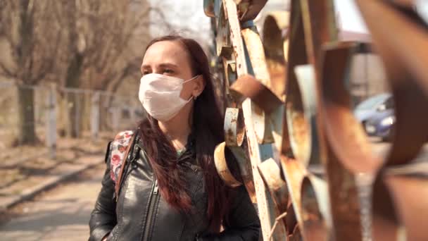 Портрет молодой женщины в медицинской маске на лице, стоящей на улице. Взрослая женщина закрыла лицо маской, чтобы защитить себя от болезней. — стоковое видео