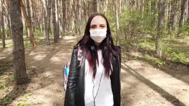 Ung kvinna med medicinsk mask i ansiktet går i skogen på frisk luft. Vuxna kvinnor täckte ansiktet med mask för att skydda sig mot sjukdomar. Begreppet hot om infektion med coronavirus. — Stockvideo