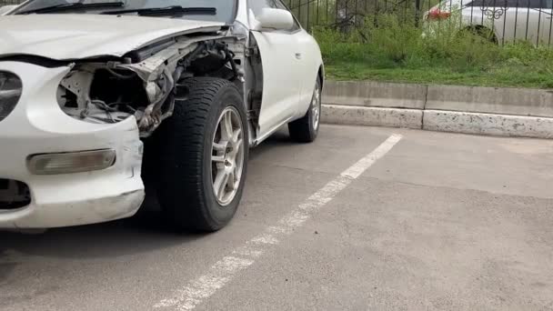 Coche blanco después de un accidente, con una capucha abollada y parachoques. Coche viejo con capó de metal arrugado estacionado en el lugar de estacionamiento pavimentado — Vídeos de Stock