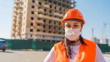 İnşaat halindeki evin arka planında maske ve tulumlu kadın inşaat işçisinin portresi var..