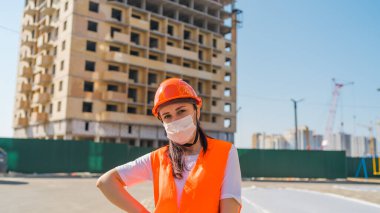 İnşaat halindeki evin arka planında maske ve tulumlu kadın inşaat işçisinin portresi var..