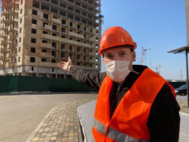 Tulumlu ve tıbbi maskeli bir adam inşaat halindeki evi işaret ediyor..