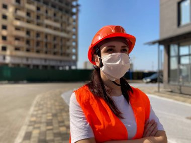 İnşaat halindeki evin arka planında maske ve tulumlu kadın inşaat işçisinin portresi var..