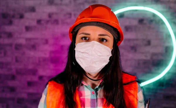 Портрет строительницы в комбинезоне и медицинская маска на подсвеченной стене. Концепция угрозы коронавирусной эпидемии . — стоковое фото