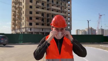 Tulumlu erkek inşaat işçisi inşaat alanında yüzüne tıbbi maske takıyor..