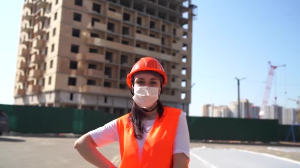 Ritratto di operaia donna in maschera medica e tuta su sfondo di casa in costruzione . — Video Stock