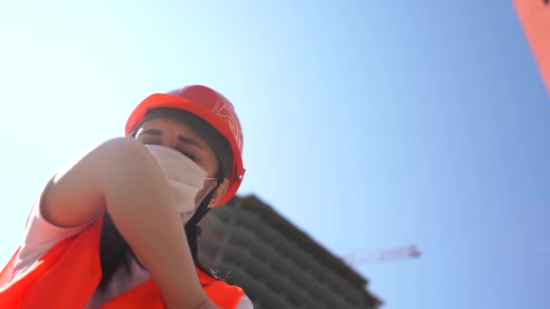 身穿工作服、戴着医疗面罩的女建筑工人手肘咳嗽在在建房屋的背景下。Coronavirus流行病感染威胁概念. — 图库视频影像