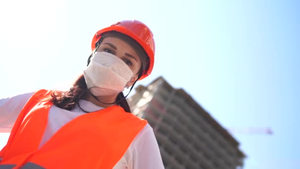 Portrait of female construction worker in medical mask and overalls on background of house under construction. — Stock Video