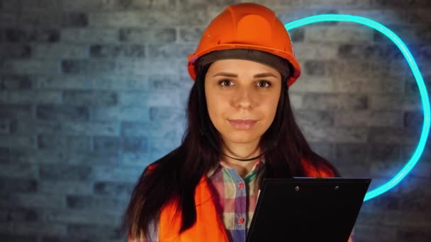 Portrét ženské stavební pracovnice v montérkách se schránkou proti osvětlené stěně. — Stock video