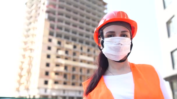 Retrato de mujer trabajadora de la construcción en máscara médica y mono sobre fondo de casa en construcción . — Vídeos de Stock