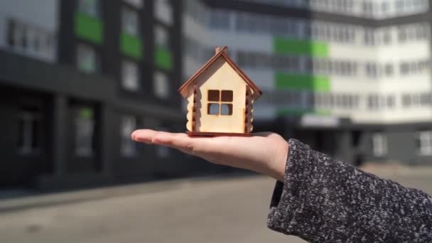 Close-up van kleine houten huis in vrouwen hand op de achtergrond van gebouwde huis. Concept van de aankoop van een nieuw appartement. — Stockvideo