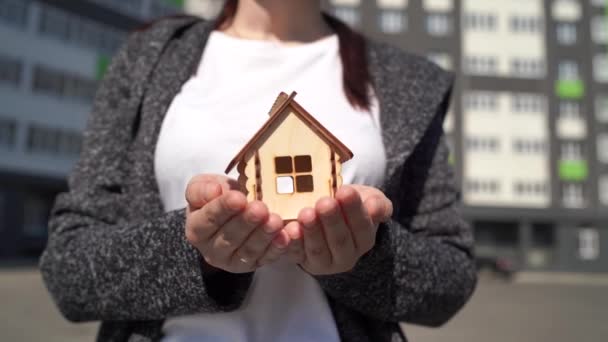 Close up de mulher segurando pequena casa de madeira em mãos no fundo da casa construída. Conceito de compra de novo apartamento. — Vídeo de Stock