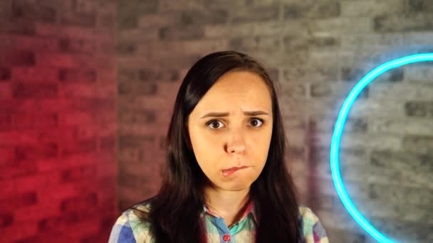 Portrait of attractive woman biting her lips resentfully against illuminated wall. — Stock Video