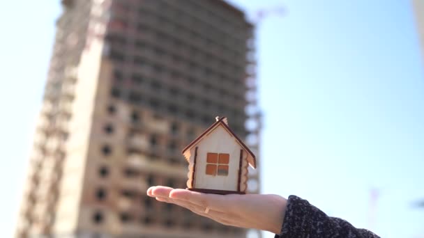 El primer plano de la pequeña casa de madera en las mujeres mano sobre el fondo de la casa en construcción. Concepto de compra de apartamento nuevo . — Vídeo de stock