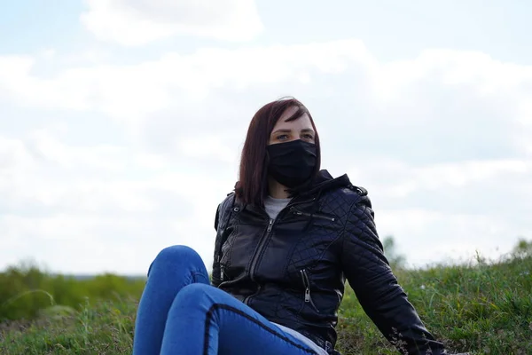 黒い医療用マスクとカジュアルな服を丘の上に曇りの日に座っている若い女性 田舎で自然を楽しみながらひとりで休む大人の女性 — ストック写真