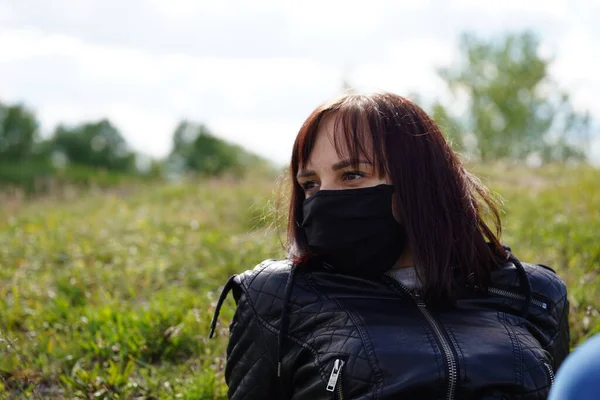 黒い医療マスクと曇りの日に丘の上に横たわるカジュアルな服で若い女性のクローズアップ 田舎で自然を楽しみながらひとりで休む大人の女性 — ストック写真