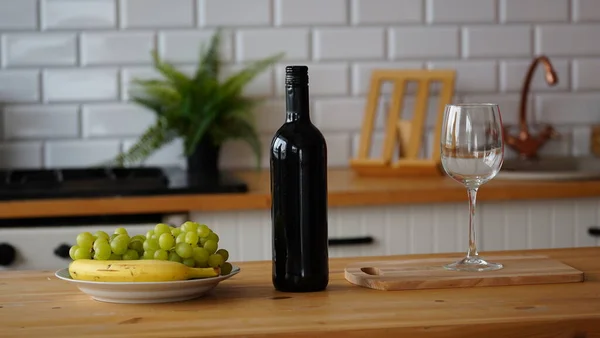 Close up of open bottle of wine and glass of wine with fruits on plate on table in kitchen. Concept of dating.