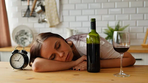 Uma mulher alcoólica dorme na cozinha de manhã, perto de uma garrafa de vinho . — Fotografia de Stock