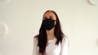 Siyah tıbbi maskeli genç bir kadın beyaz desenli duvara karşı renkli halteri kaldırıyor. Yetişkin kadın spor yapıyor, Coronavirüs salgını sırasında evde izole ediliyor..