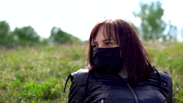 Primer plano de la mujer joven con máscara médica negro y ropa casual que yace en la colina en el día nublado. Mujer adulta descansando sola, disfrutando de la naturaleza en el campo . — Vídeo de stock