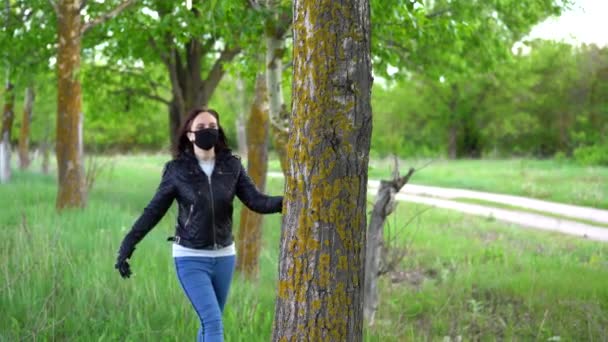 Jonge vrouw in zwart medisch masker en handschoenen knuffelende boom in het bos. Volwassen vrouw genietend van de natuur op het platteland in de periode van de besmetting met het coronavirus. — Stockvideo