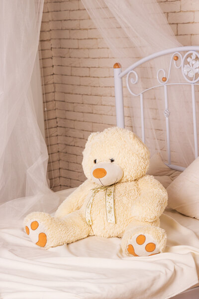 Белый плюшевый мишка на кровати
