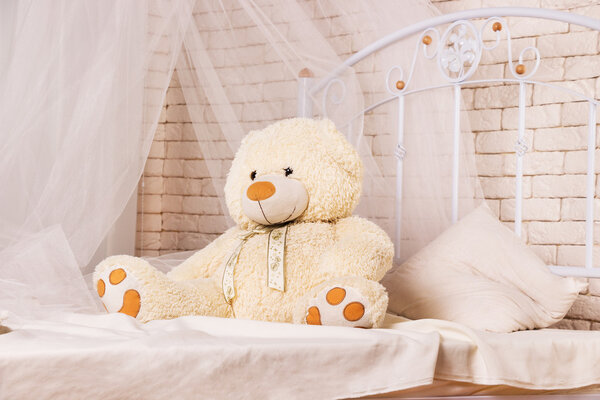 Белый плюшевый мишка на кровати
