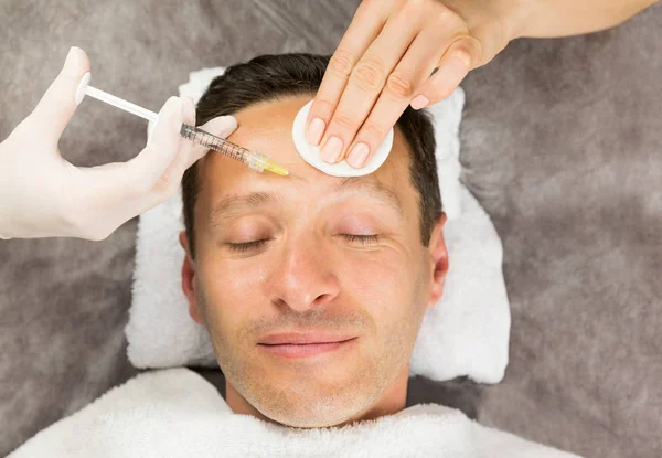 Face of laying man, hands of beautician with a syringe and sponge