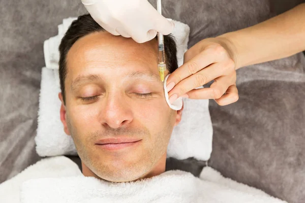 Face of laying man, hands of beautician with a syringe and sponge