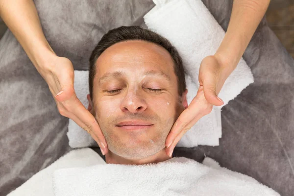 Male face with cream mask, hands of professional beautician — Stock Photo, Image