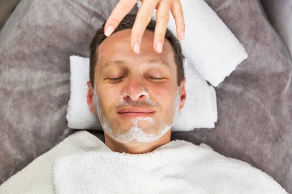 Mannelijke gezicht met crème-masker, handen van professionele schoonheidsspecialist — Stockfoto