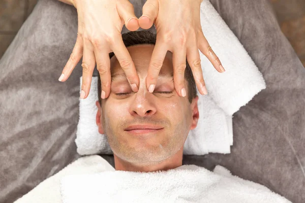 Mannelijke gezicht met crème-masker, handen van professionele schoonheidsspecialist — Stockfoto