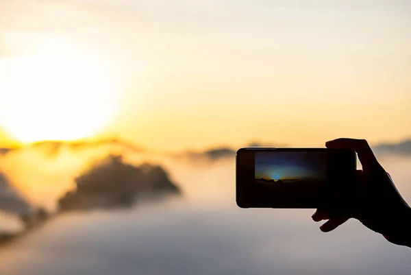 Mano sosteniendo el teléfono disparando el sol de la mañana y la niebla. — Foto de Stock